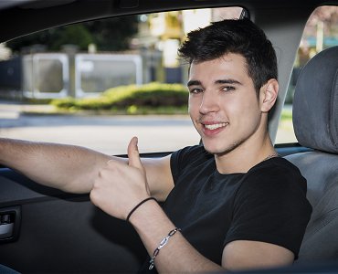 Young male driving lesson student with thumbs up sat in car learning to drive