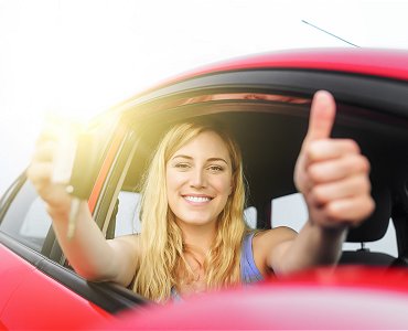 Young female driving lesson student sat in car with thumbs up